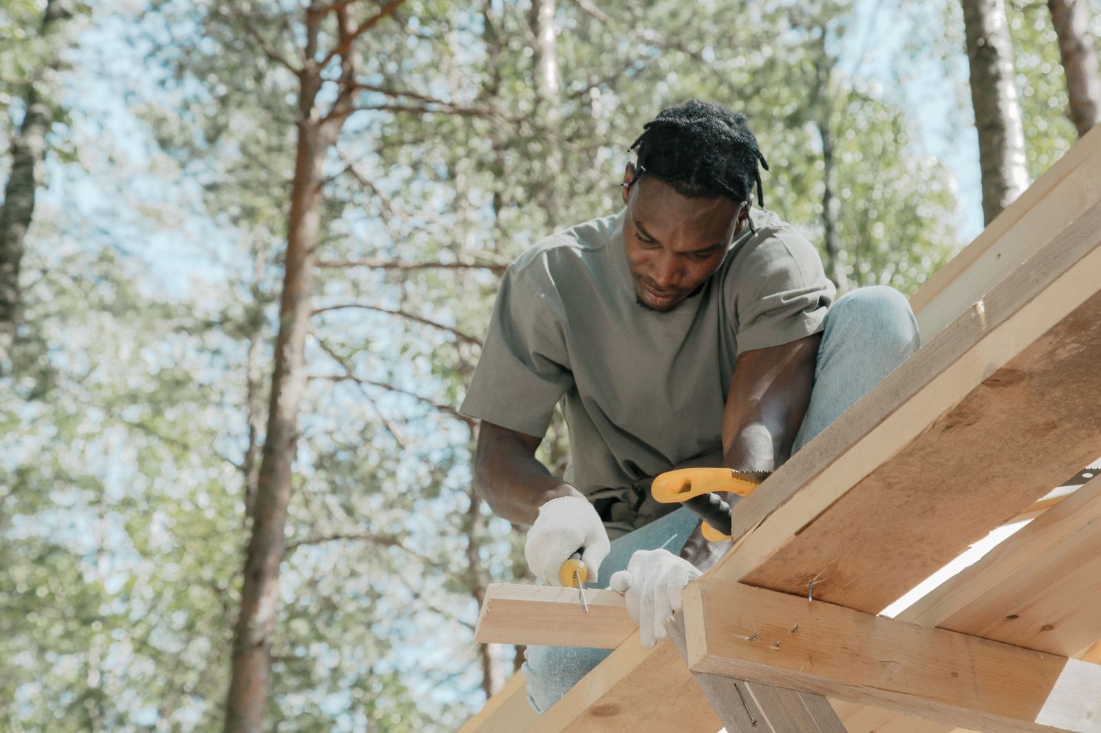Carpenter in work gloves cutting a pine board with a circular saw on a timber frame outdoors