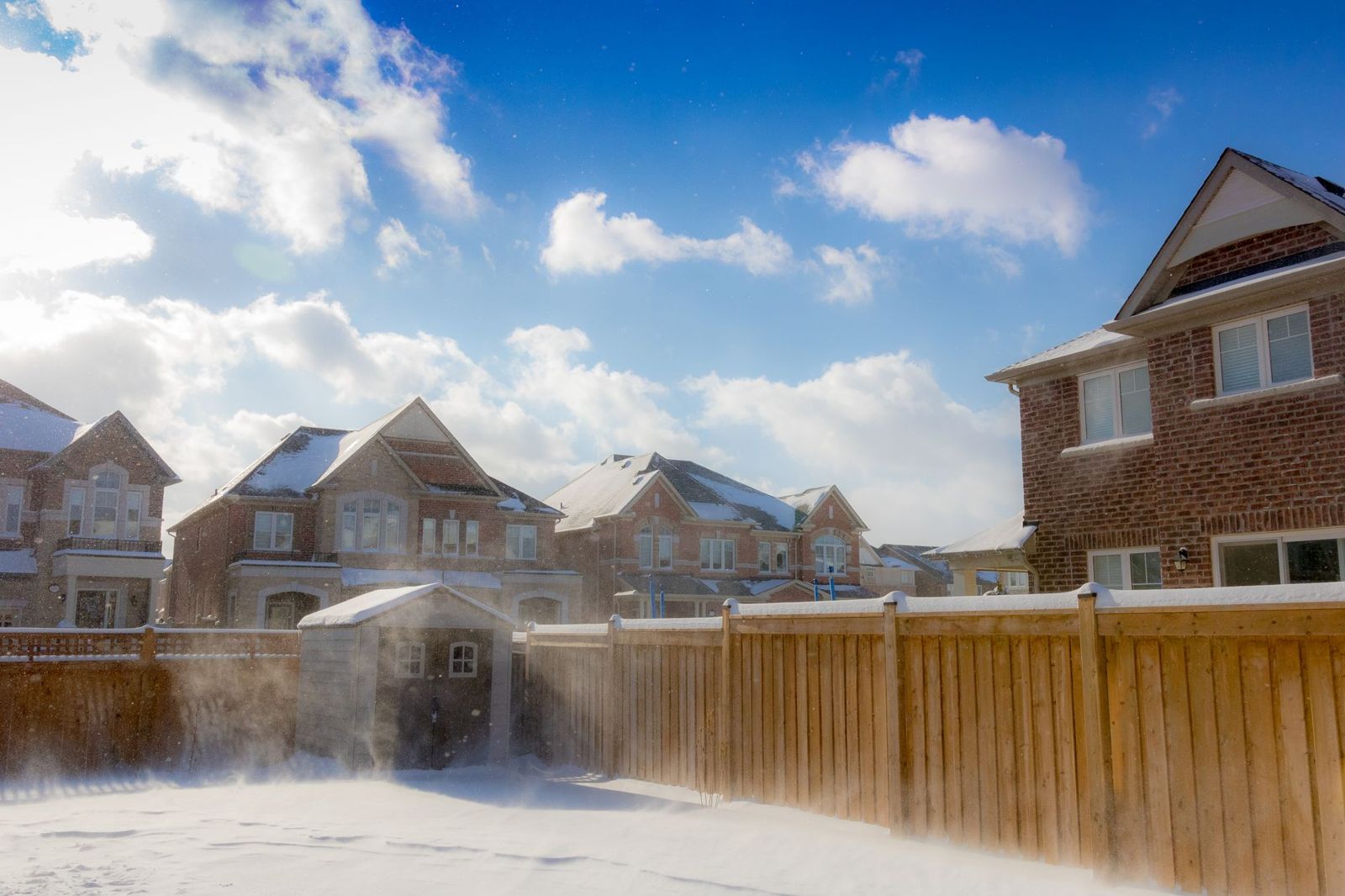 Tall board-on-board wood privacy fence enclosing a snowy back yard in a row of suburban brick houses