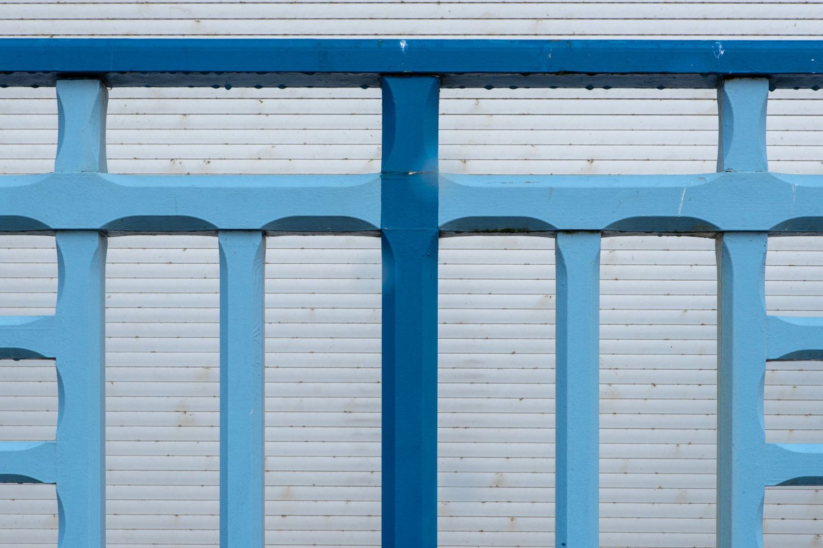 Blue painted metal railing with vertical and horizontal bars in front of white horizontal siding