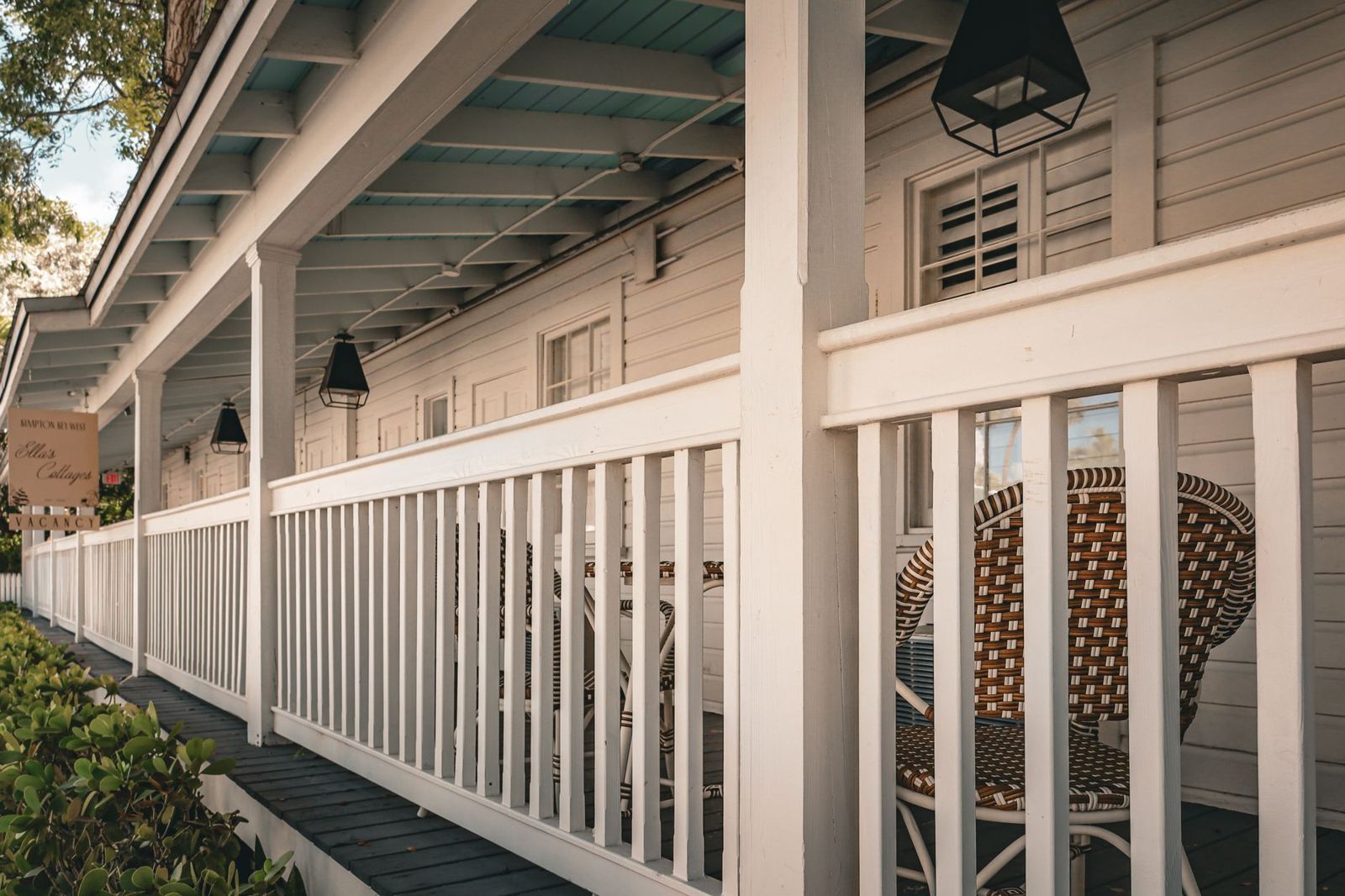 White painted porch railing with square balusters along a covered porch with lanterns and wicker chairs