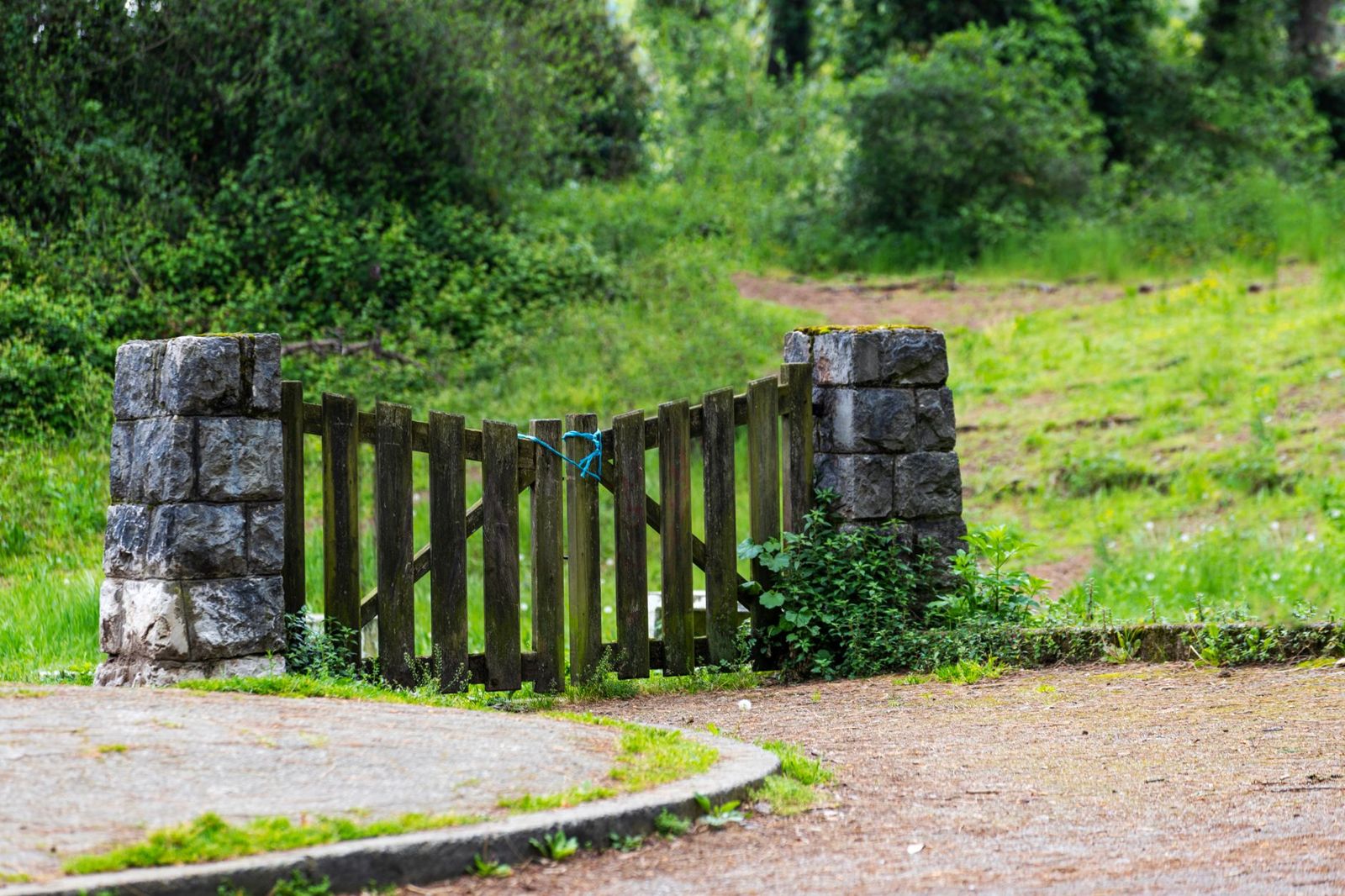 Weathered wooden picket gate between two rough stone pillars on the edge of a grassy lot